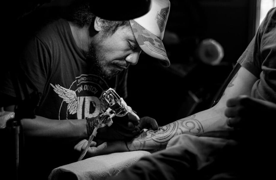 black and white photo of a man tattooing someones arm